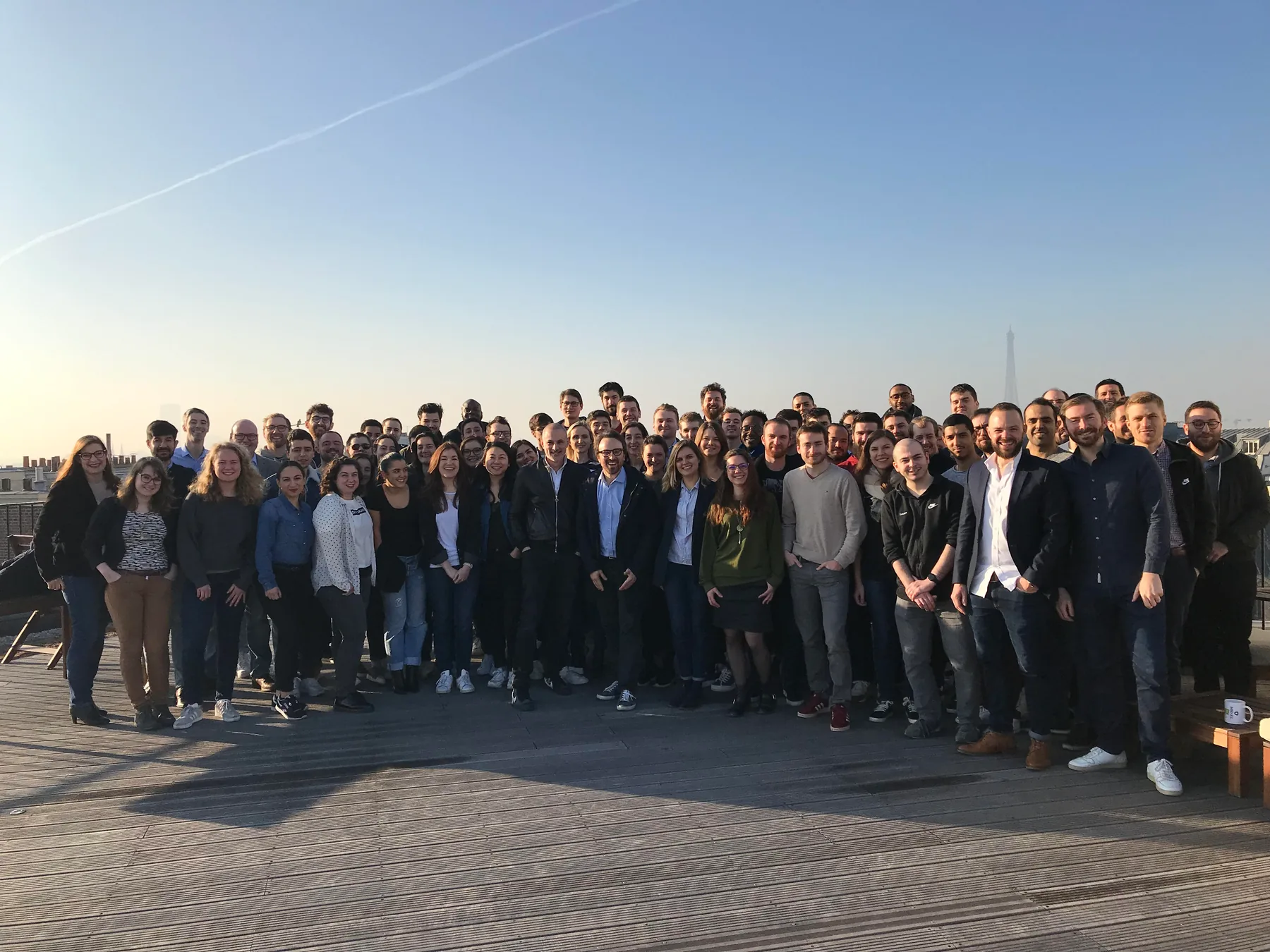 Large group of Mirakl Paris team members posing together on a rooftop terrace at dusk, with the Eiffel Tower visible in the background