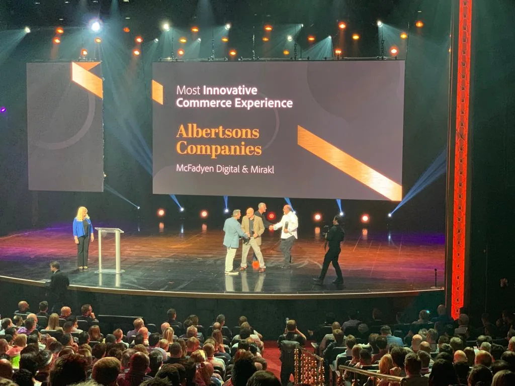 Award ceremony on a large stage with attendees in the audience. The screen displays 'Most Innovative Commerce Experience — Albertsons Companies — McFadyen Digital & Mirakl'. Several people on stage shake hands as the award is presented.