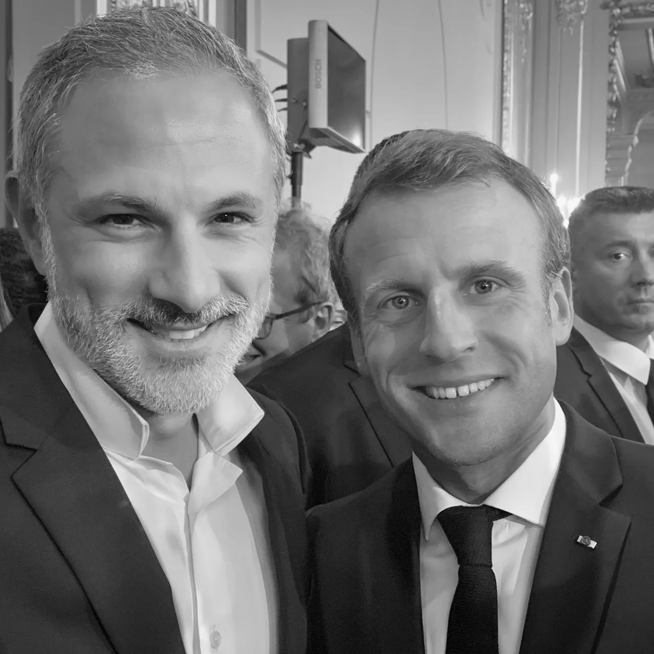 Black-and-white photo of two men posing together and smiling at an indoor event