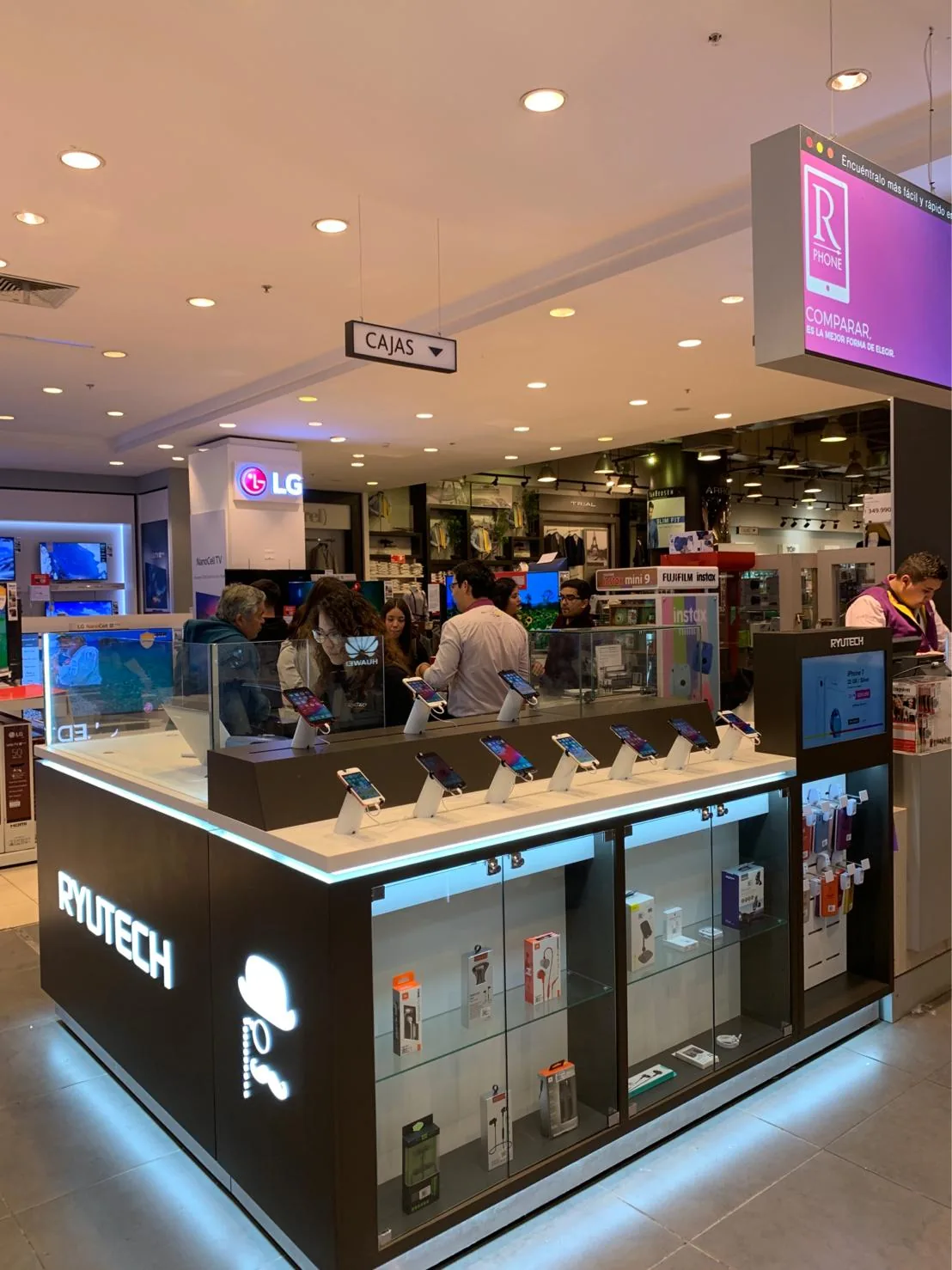 Interior photo of a Ryutech electronics kiosk inside a Ripley department store in Chile, with smartphones on display stands, glass cases of accessories, and shoppers browsing, with LG and Fujifilm brand signage visible in the background