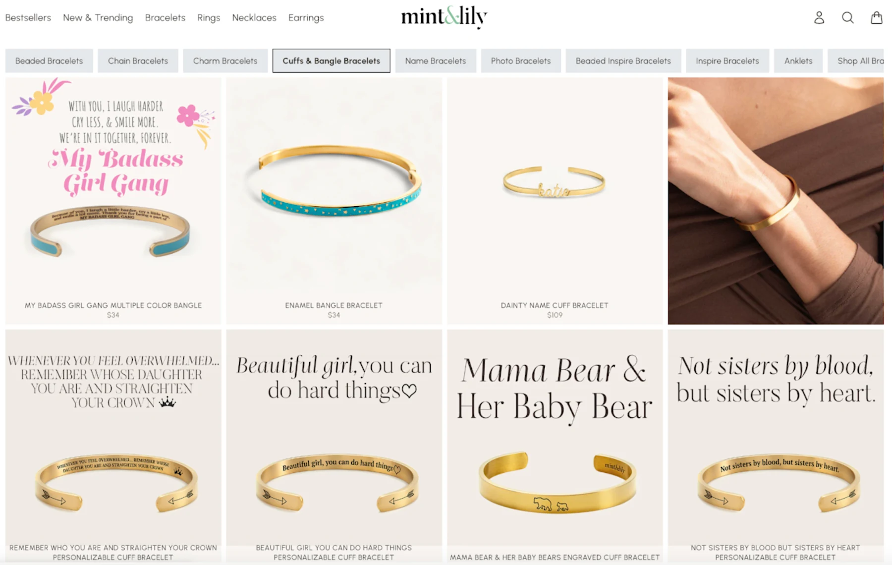 Screenshot of the Mint & Lily website showing the Cuffs & Bangle Bracelets category page. Visible products include personalized engraved gold cuff bracelets with inspirational messages such as "My Badass Girl Gang," "Mama Bear & Her Baby Bear," and "Not sisters by blood, but sisters by heart," priced from $34 to $109.