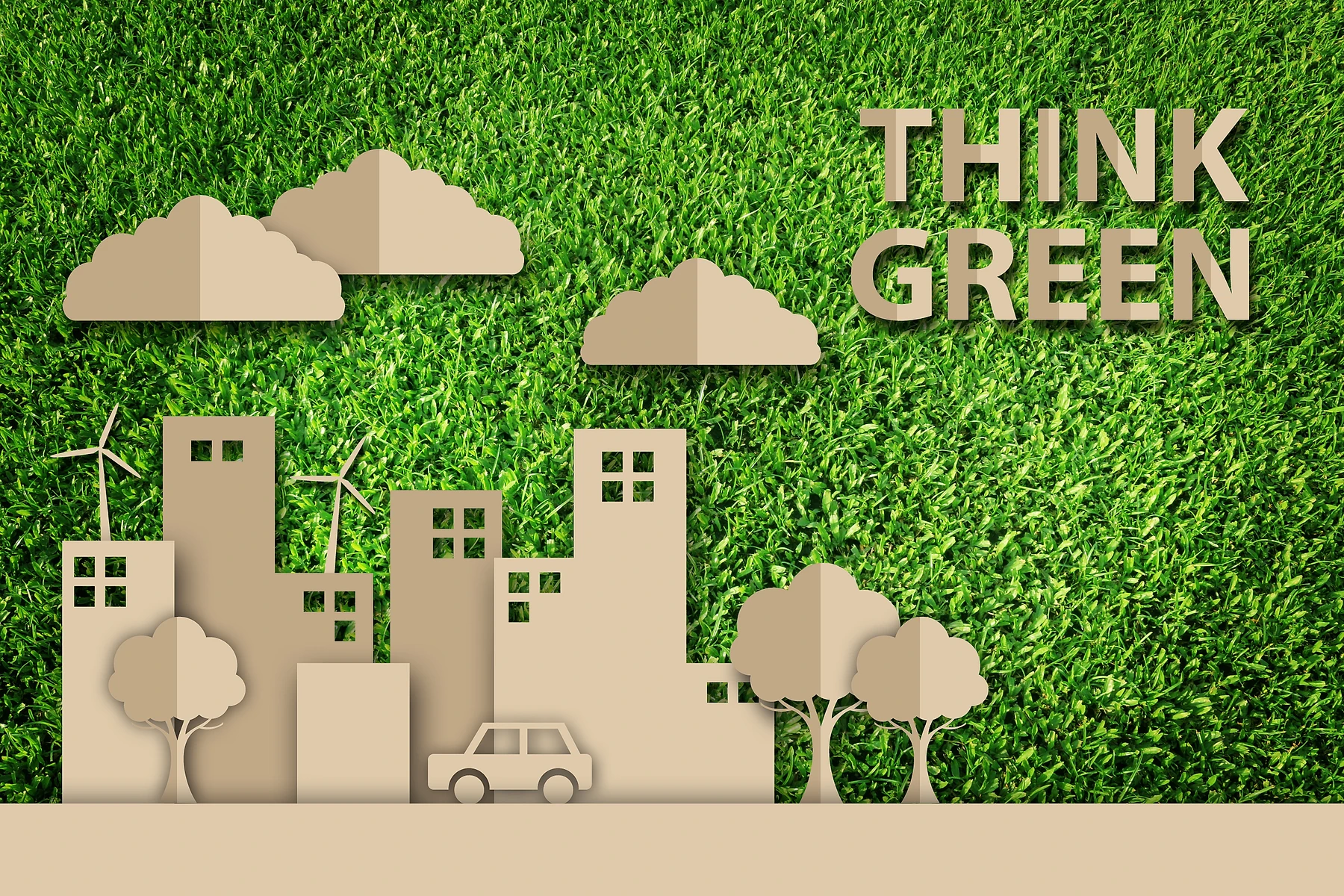 Paper cut-out style illustration of a green cityscape with buildings, wind turbines, trees, clouds, and a car, with the text 'Think Green' overlaid on a grass background.