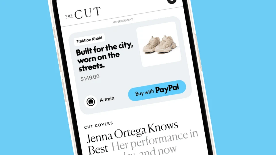 A smartphone showing The Cut editorial website with a sponsored product ad for Traktion Khaki sneakers at $149 and a "Buy with PayPal" button — an example of off-site retail media running on a publisher.